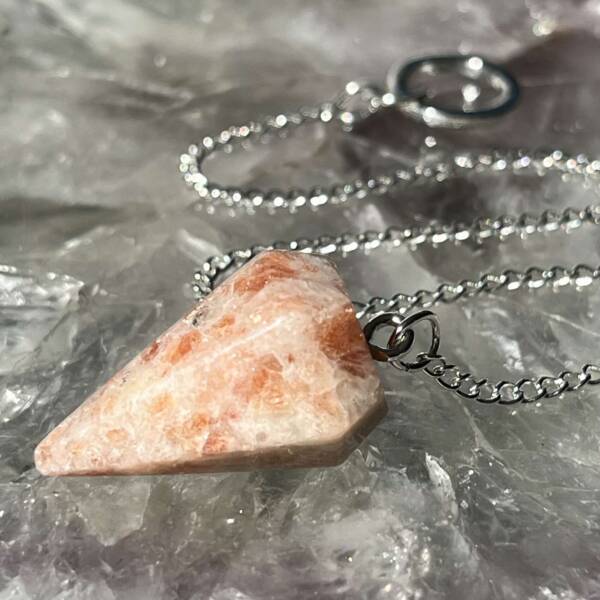 sunstone pendulum, opaque pale creamy orange with bright shiny flashes and a white metal chain with ring