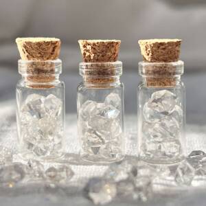 natural herkimer diamonds ten to a clear glass, corked bottle, a double terminated natural form of clear quartz